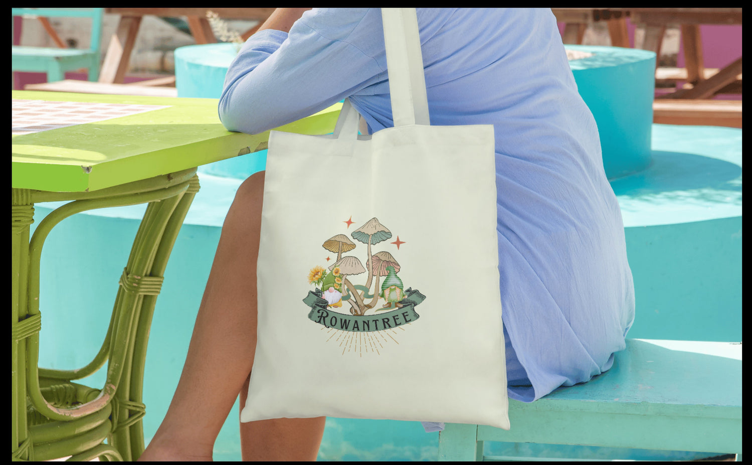 Person sitting with handbag over their shoulder. Handbag has a whimsical scene of gnomes and mushrooms printed on it.