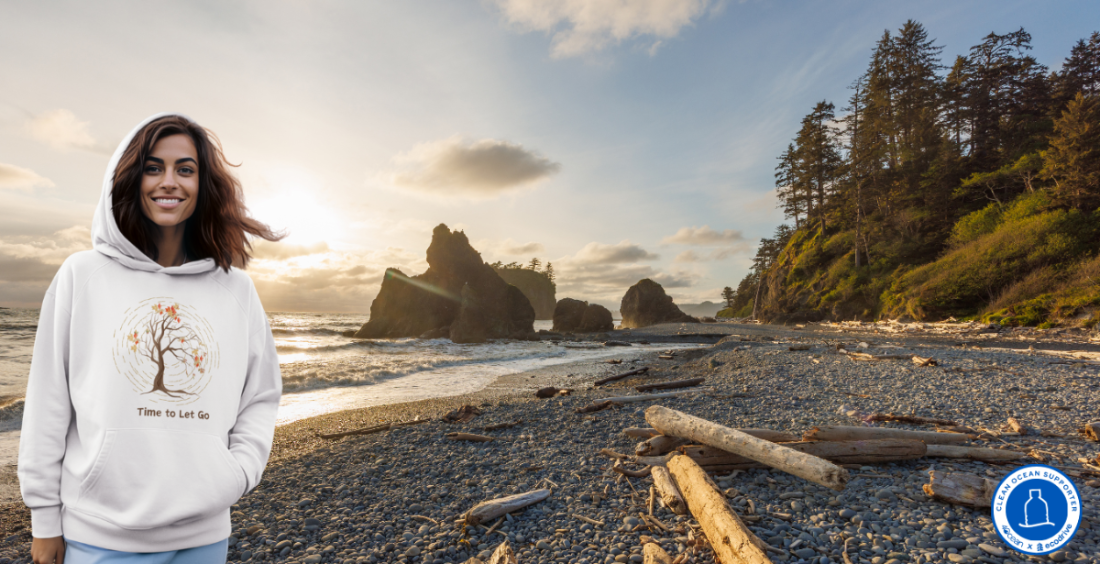 Woman in a white hoodie with a tree design on a beach at sunset