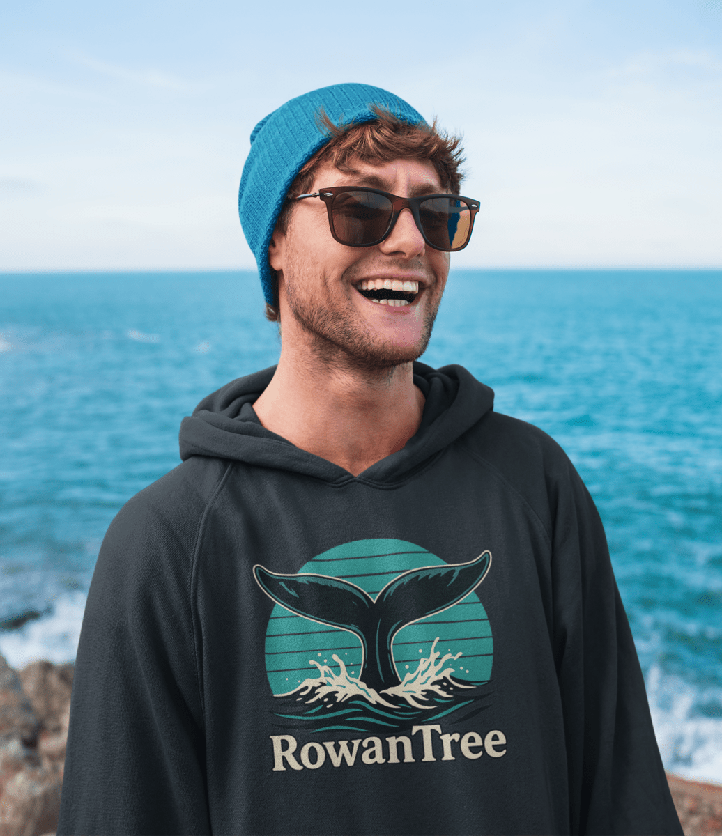 RowanTree Whale Song Pullover Hoodie - RowanTree ClothingMan wearing a hoodie with RowanTree whale design, by the ocean