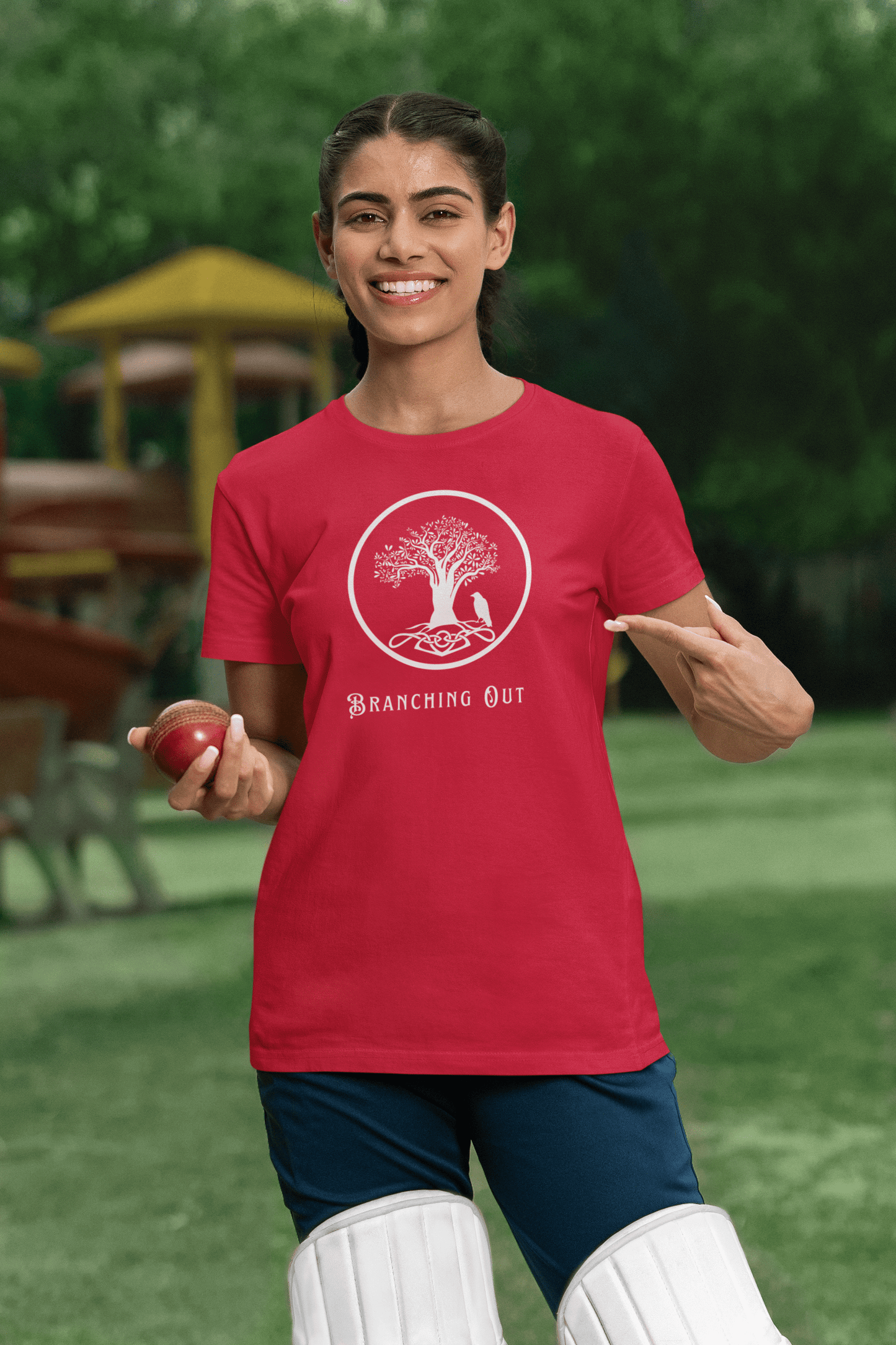 Woman on a cricket pitch wearing a red bamboo with a Celtic style tree and crow logo