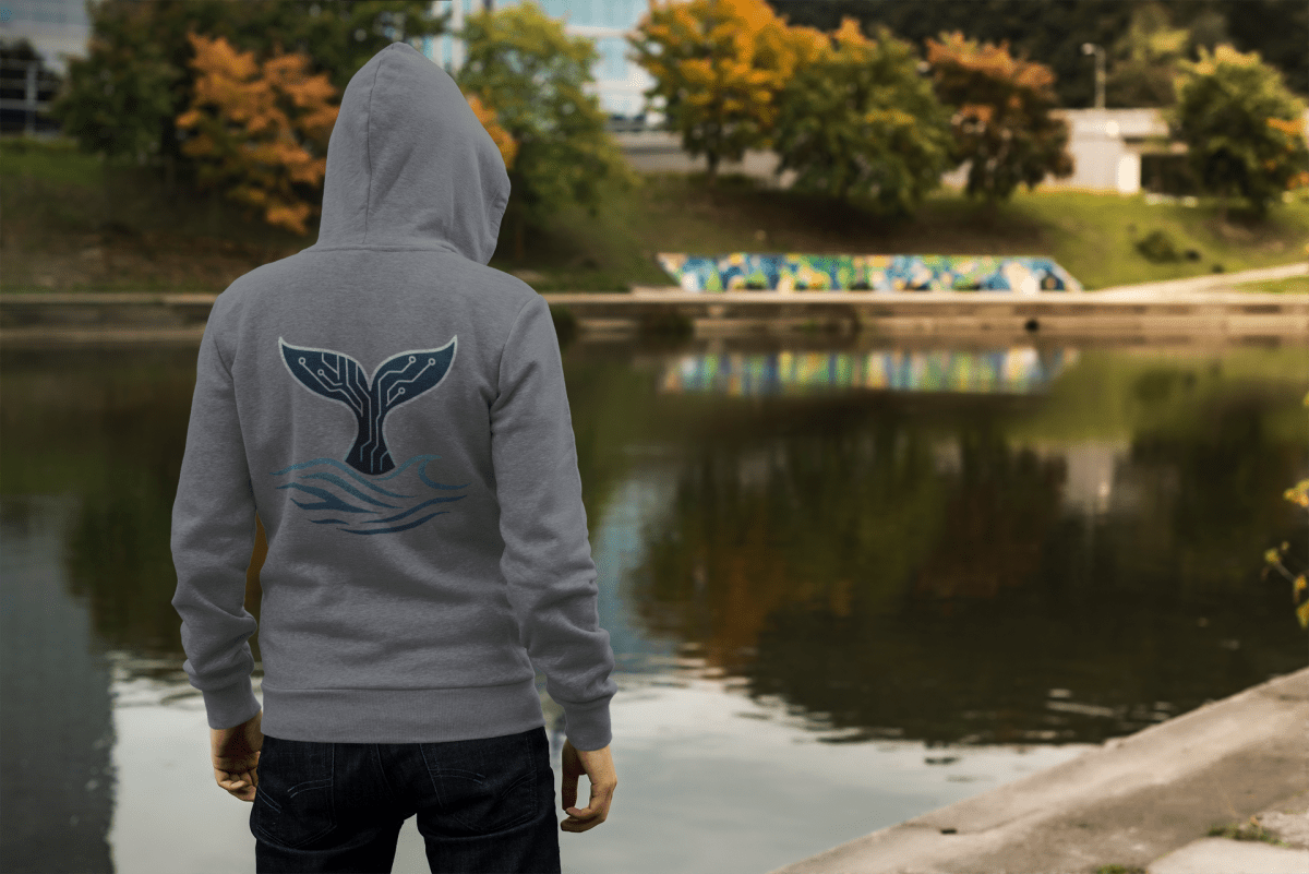 Man wearing the RowanTree Whale Circuitry hoodie overlooking a lake, symbolizing harmony between technology and nature.