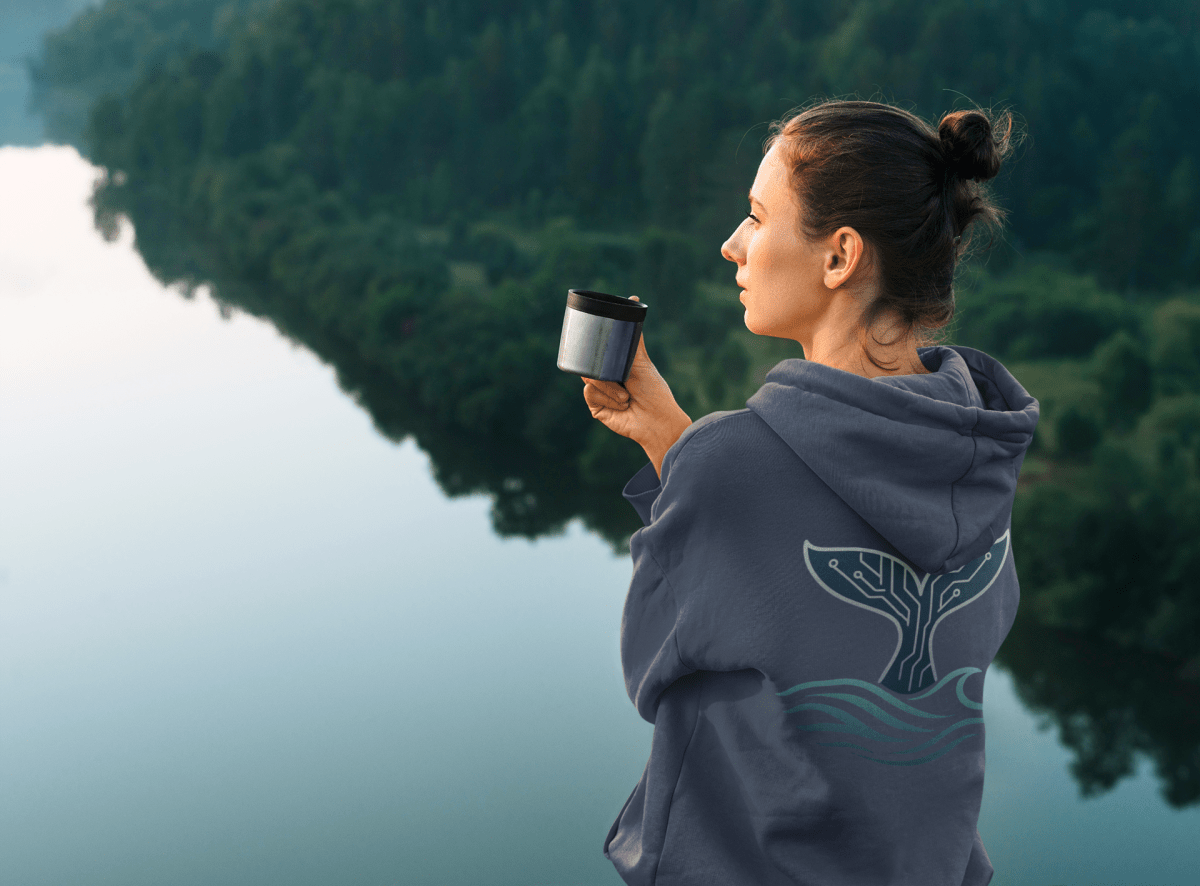 Woman wearing the RowanTree Whale Circuitry  hoodie overlooking a lake, symbolizing harmony between technology and nature.